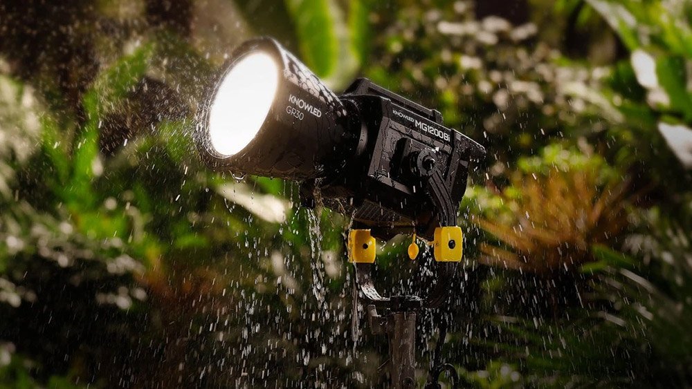 Освітлювач Godox KNOWLED MG1200Bi працює під сильною зливою на відкритій локації в сутінках: потоки води стікають по корпусу й рефлектору GR30, демонструючи заявлену вологозахищеність